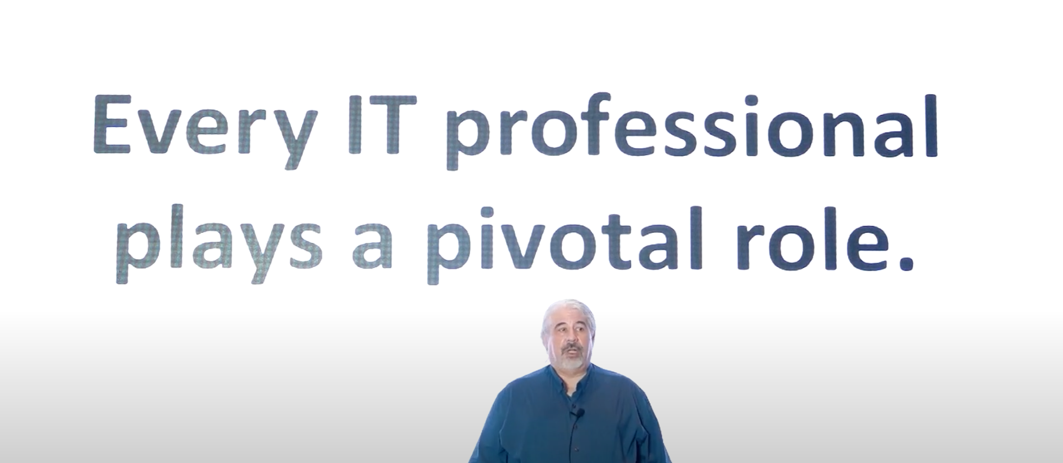 Speaker with a screen behind them stating that "Every IT Professional plays a pivotal role"